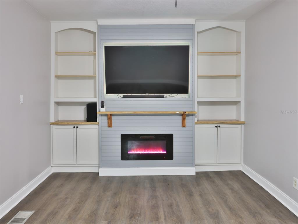 A living room features a wall-mounted television above an electric fireplace and built-in shelving — 3016 N MARYLAND AVENUE, PLANT CITY, FL