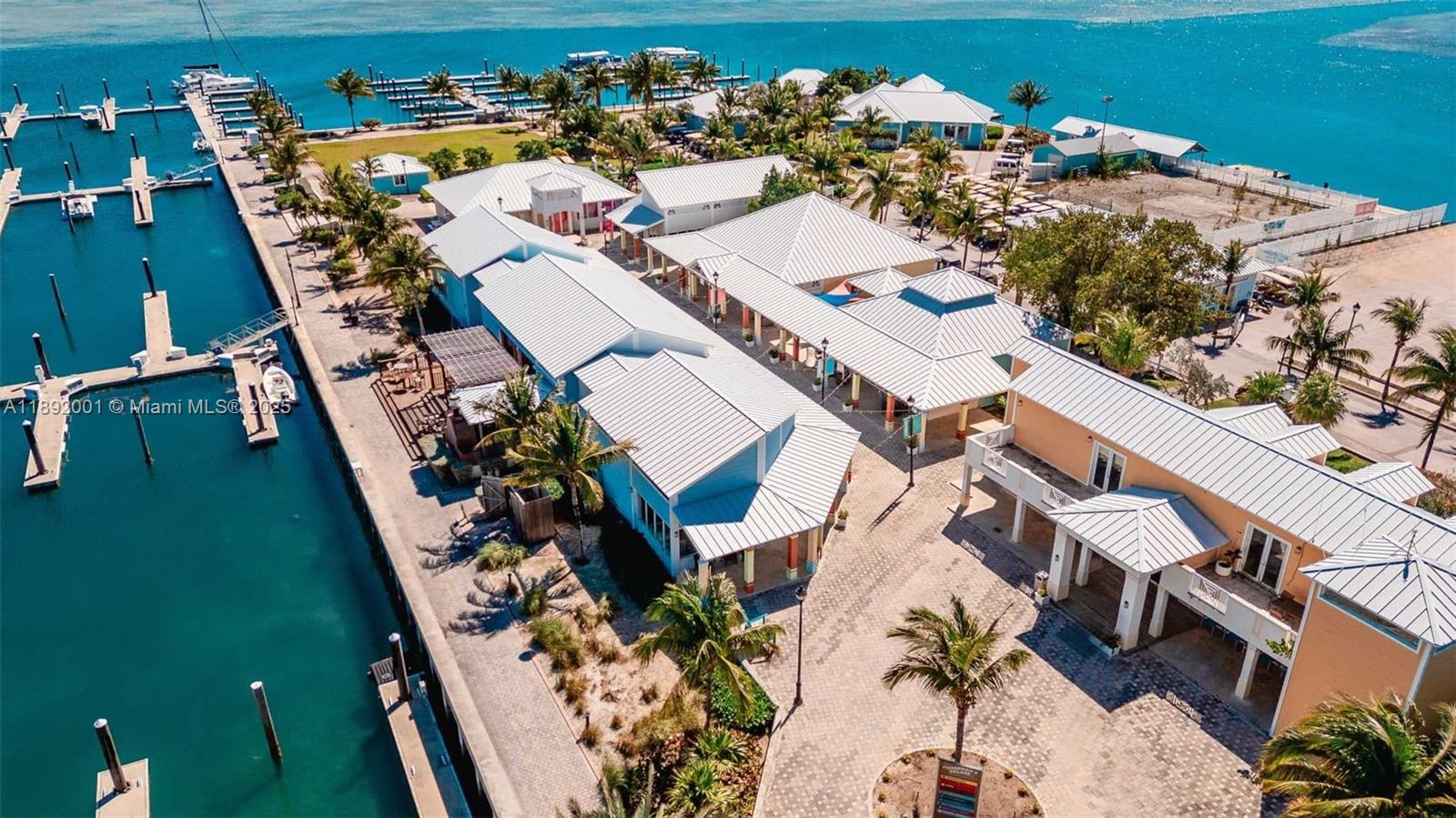 An aerial view shows a waterfront complex with multiple buildings, palm trees, and boat slips — Dolphin # 8 Fisherman Village Marina., ., .