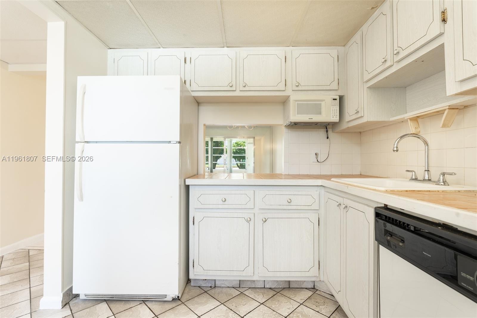 A kitchen features white cabinets, a white refrigerator, a black dishwasher, and tiled countertops — 7877 Golf Cir Dr # 108, Margate FL 33063, MARGATE, FL