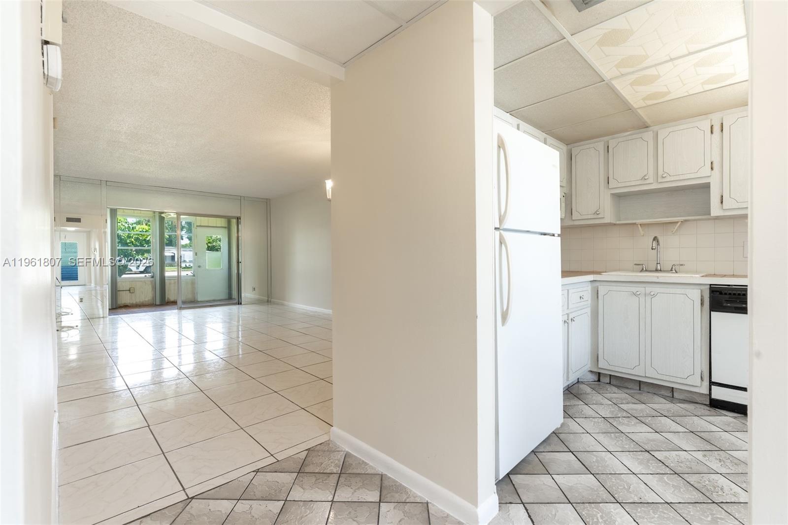 A kitchen with white cabinets and tile floors opens into a bright, tiled living area — 7877 Golf Cir Dr # 108, Margate FL 33063, MARGATE, FL