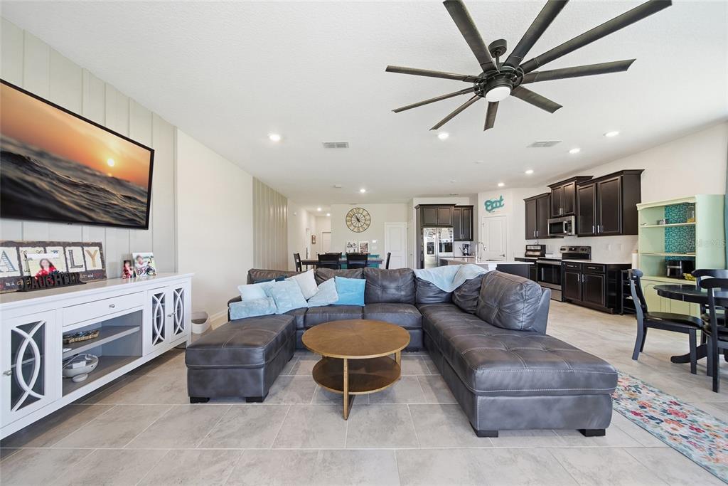 An open-concept living room features a gray sectional sofa, a television, and an adjacent kitchen — 13 WHITE HORSE WAY, GROVELAND, FL