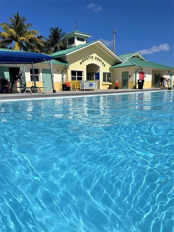 A swimming pool sits in front of a yellow building labeled Aquatic Center — 2611 NE 20th Street, Pompano Beach FL 33062, POMPANO BEACH, FL