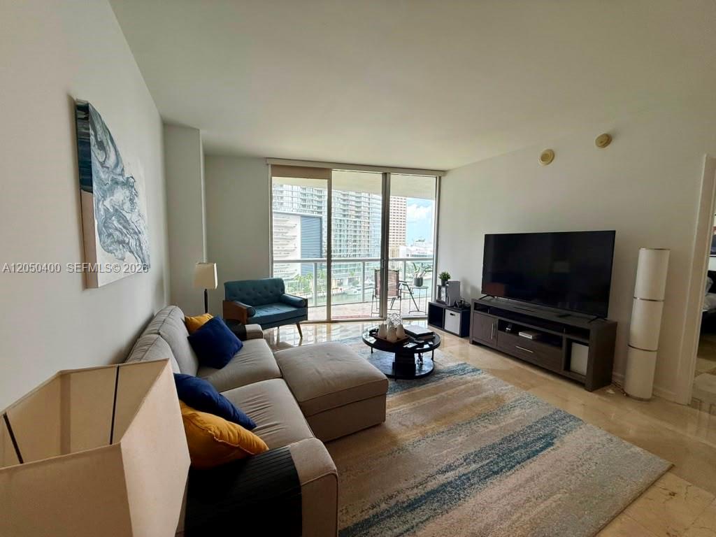 A living room features a sectional sofa, a television on a console, and a balcony view — 475 Brickell Ave # 1012, Miami FL 33131, MIAMI, FL
