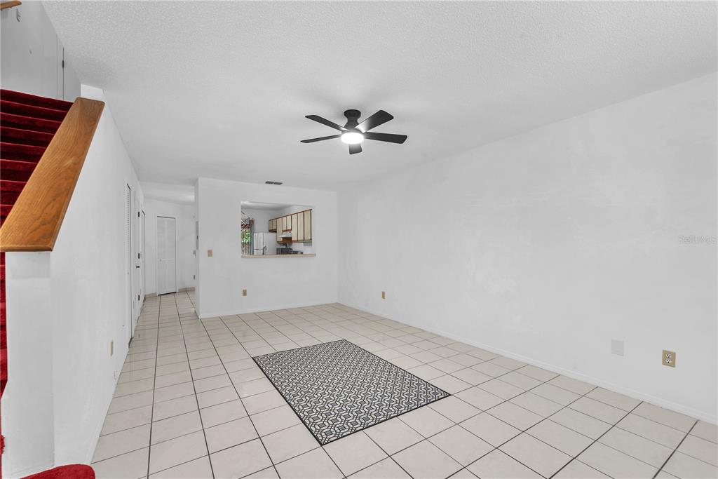 A living room with white walls, tile flooring, a ceiling fan, and a staircase — 5100 BURCHETTE ROAD UNIT 1004, TAMPA, FL