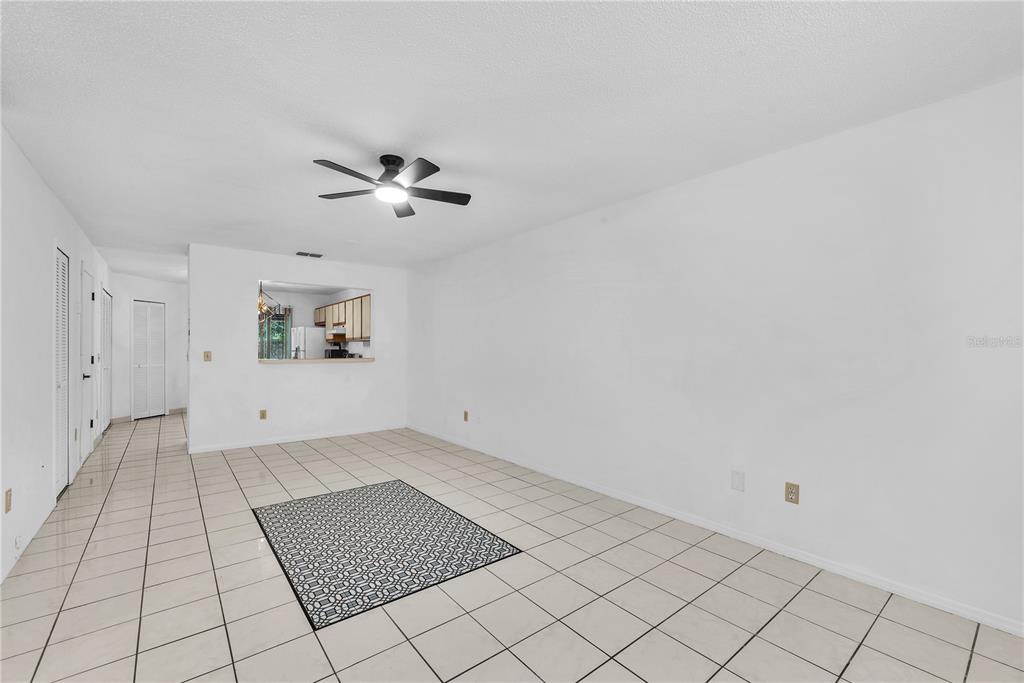 An empty room with white walls, tiled floors, a ceiling fan, and a kitchen pass-through — 5100 BURCHETTE ROAD UNIT 1004, TAMPA, FL