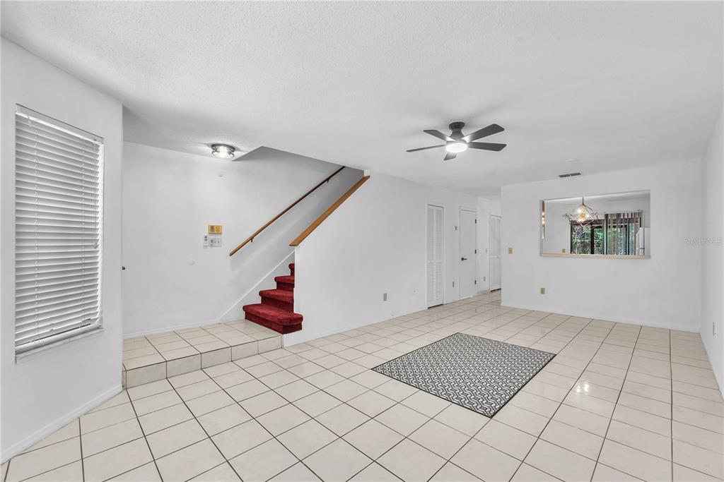 An open living area features white walls, light tile flooring, and a red-carpeted staircase — 5100 BURCHETTE ROAD UNIT 1004, TAMPA, FL
