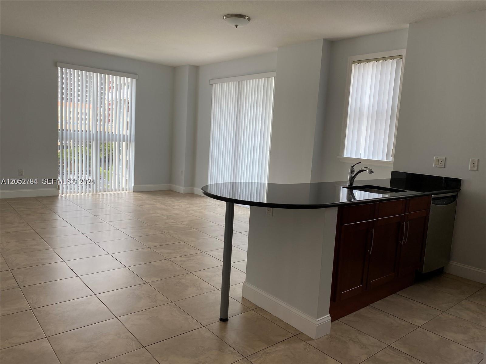 An open-concept living area features tile flooring, a kitchen island with dark cabinets, and windows — 7280 SW 90th St # 501, Miami FL 33156, MIAMI, FL