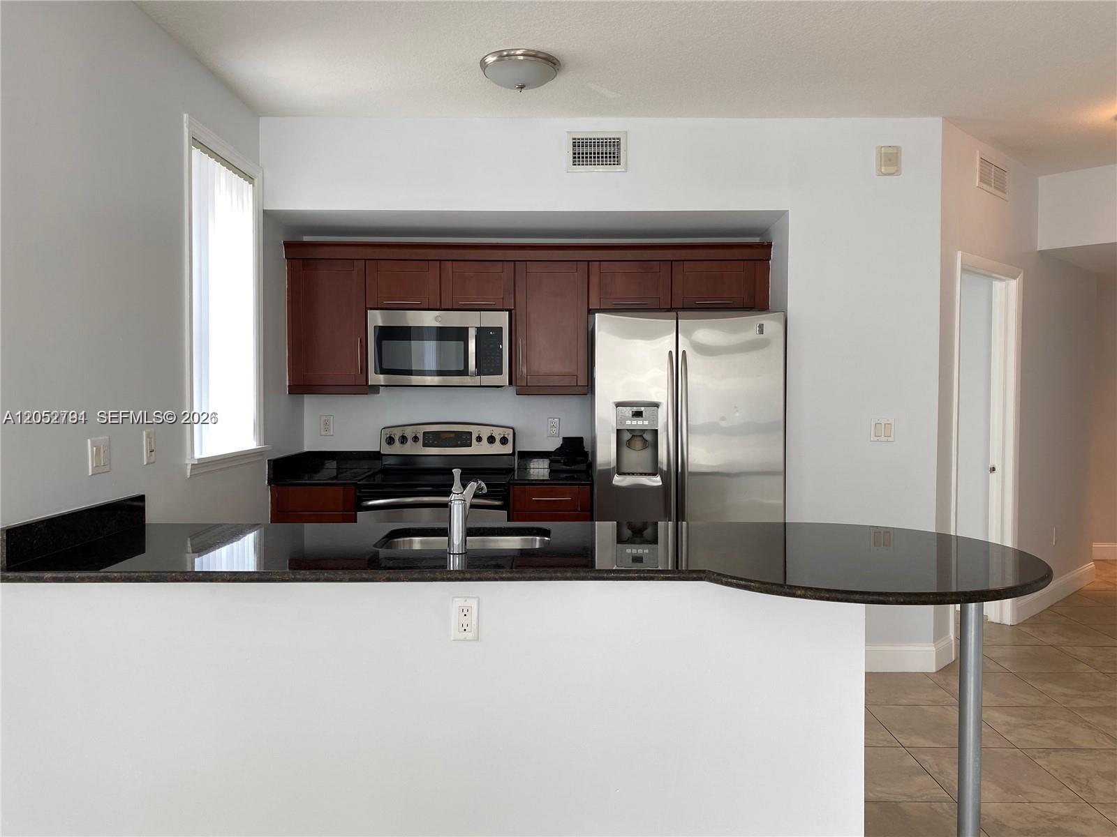 A kitchen features dark wood cabinets, stainless steel appliances, and a black granite breakfast bar — 7280 SW 90th St # 501, Miami FL 33156, MIAMI, FL
