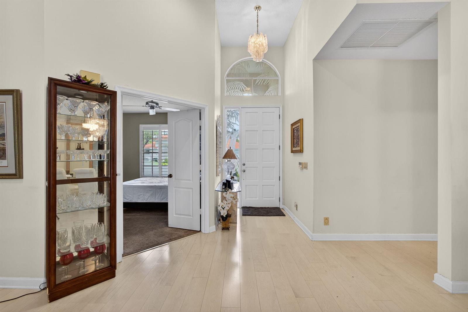 A foyer with light wood flooring, a glass display cabinet, and a white front door — 200 Eagleton Estates Boulevard, Palm Beach Gardens FL 33418, PALM BEACH GARDENS, FL