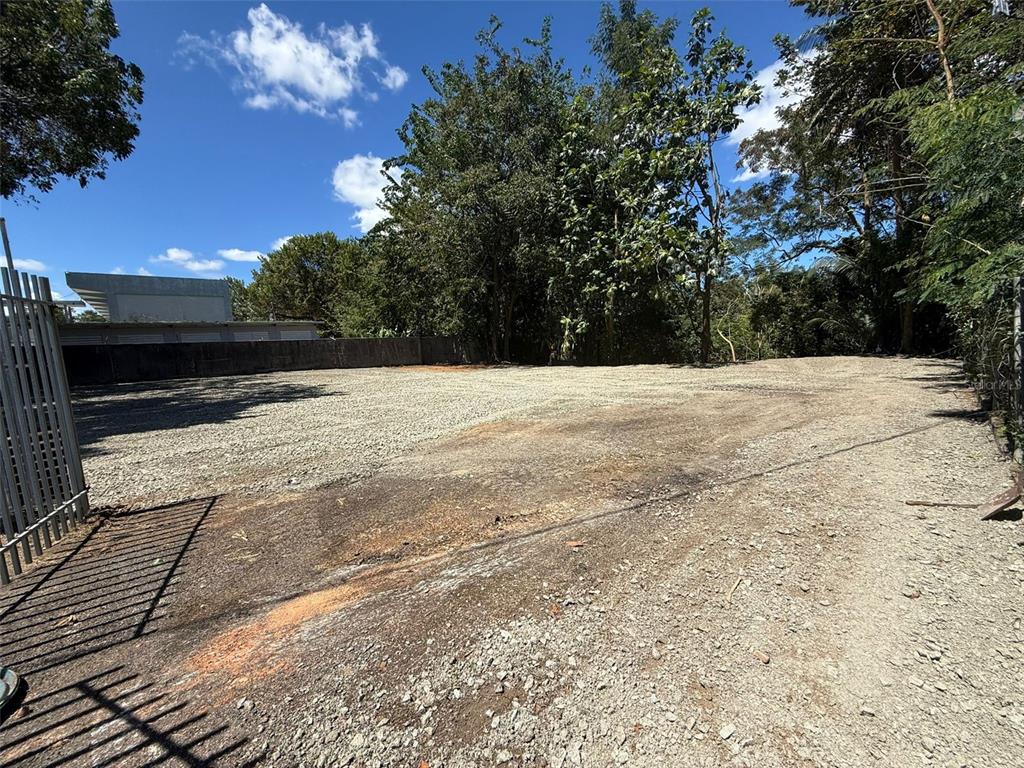 A gravel-covered vacant lot is enclosed by a metal fence and a concrete wall — SECTOR LA ALDEA, BAYAMON, PR