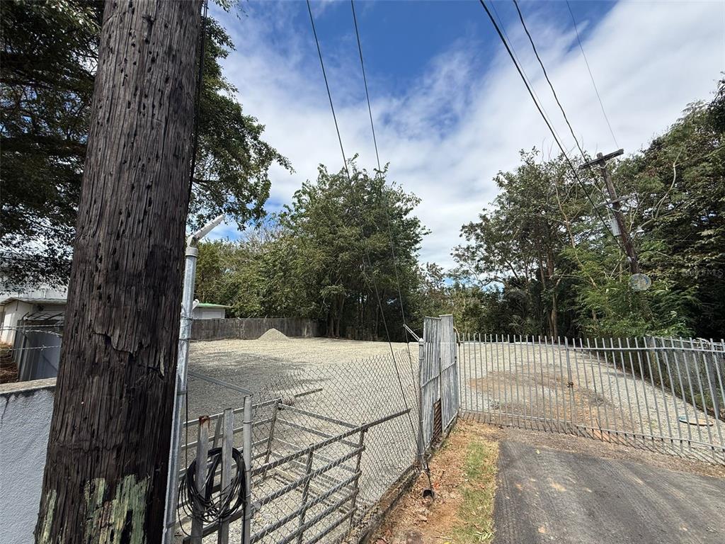 A fenced, gravel-covered lot features a utility pole and overhead power lines — SECTOR LA ALDEA, BAYAMON, PR