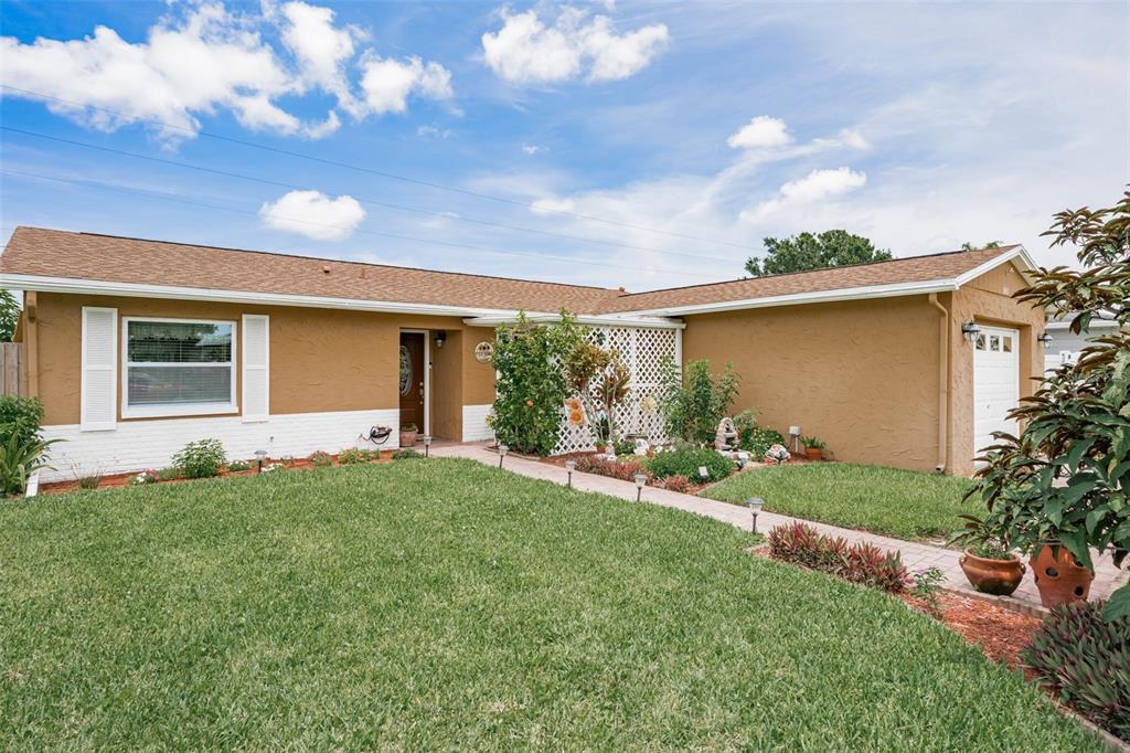 A single-story house with a brown stucco exterior, white brick base, and a front lawn — 6411 ELMHURST COURT, PINELLAS PARK, FL
