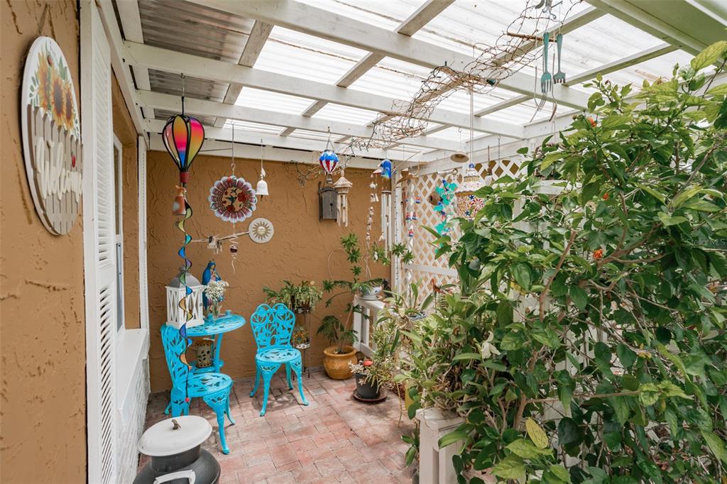 A covered patio features brick flooring, turquoise metal furniture, and various hanging garden decorations — 6411 ELMHURST COURT, PINELLAS PARK, FL
