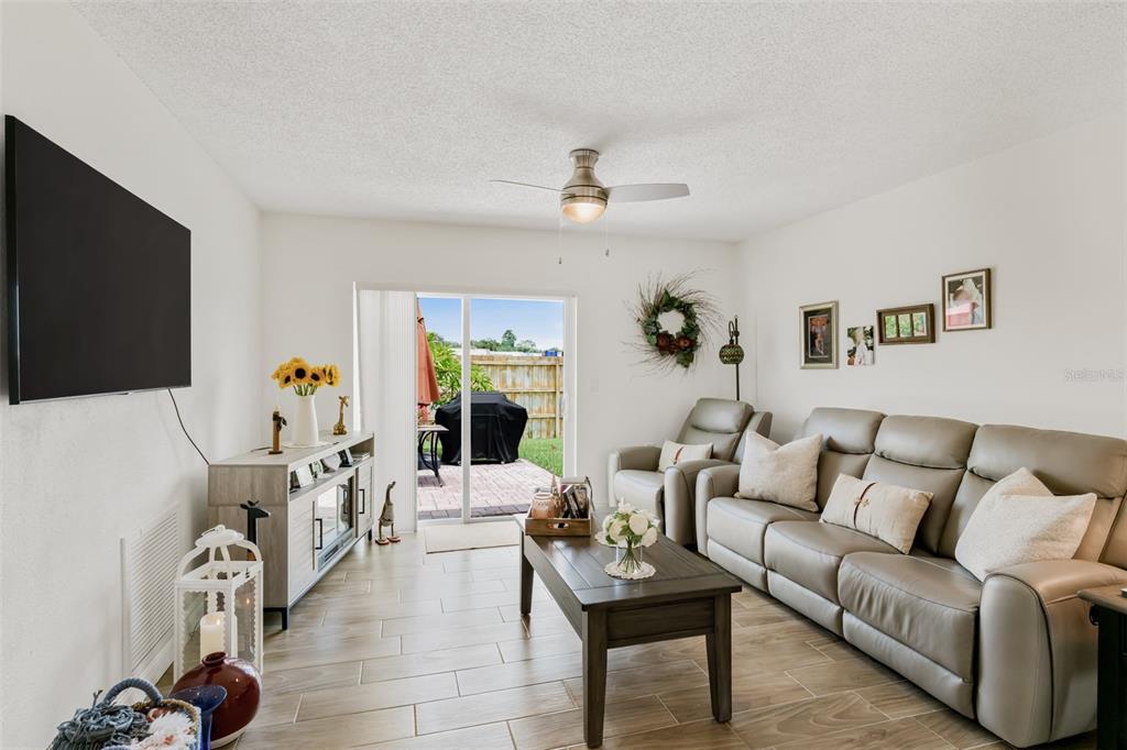 A living room with light tile flooring, a gray sofa, and a sliding glass door — 6411 ELMHURST COURT, PINELLAS PARK, FL