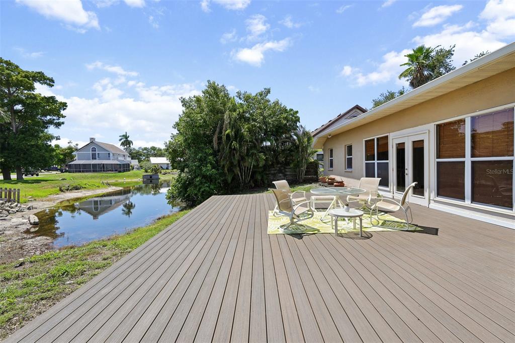 A wooden deck overlooks a small pond with patio furniture set on a green rug — 4919 32ND AVENUE DRIVE W, BRADENTON, FL