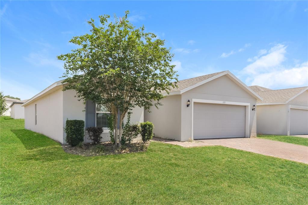 A single-story house with a beige exterior, a two-car garage, and a front yard tree — 1373 LUCERNE LOOP ROAD NE, WINTER HAVEN, FL