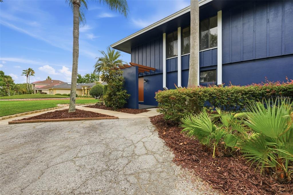 A blue two-story house features a wooden pergola over the entrance and a cracked driveway — 29116 BEAUCLAIRE DRIVE, TAVARES, FL