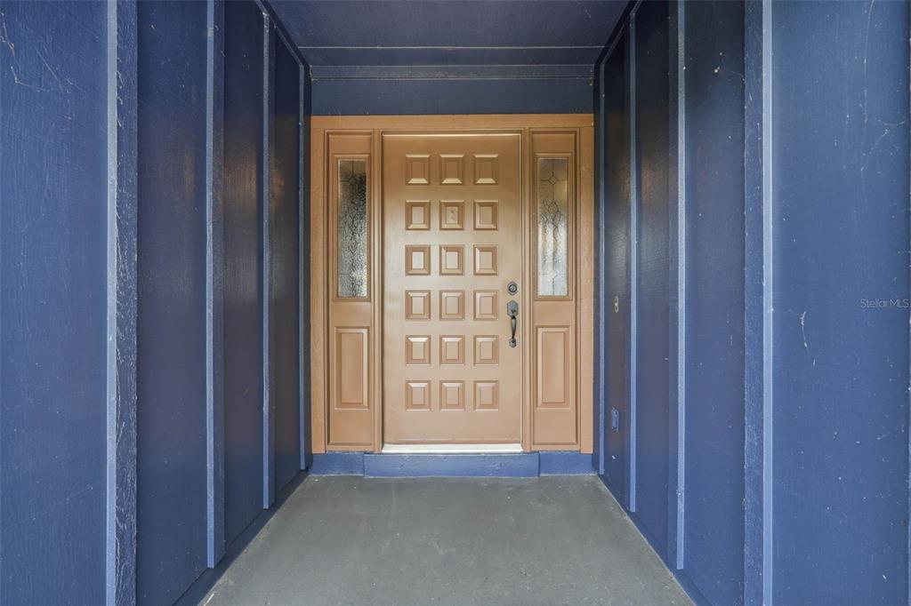 A tan front door with a grid pattern is flanked by sidelights in a blue entryway — 29116 BEAUCLAIRE DRIVE, TAVARES, FL