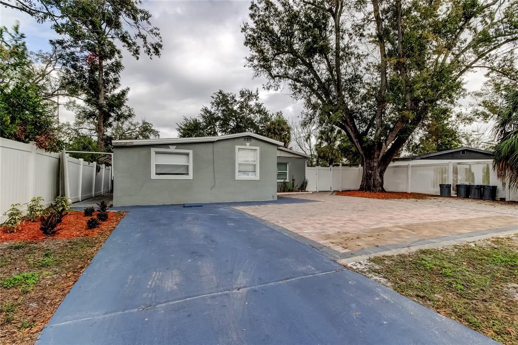 A gray single-story house features a blue concrete driveway and a paved patio area — 4532 DEVONSHIRE ROAD, TAMPA, FL
