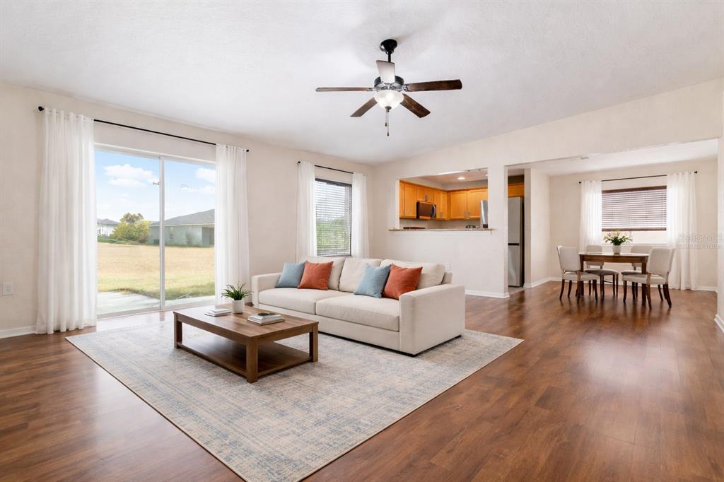 A living room with wood-look flooring, a beige sofa, and an adjacent dining area — 1131 HIGHLAND MEADOWS STREET, DAVENPORT, FL