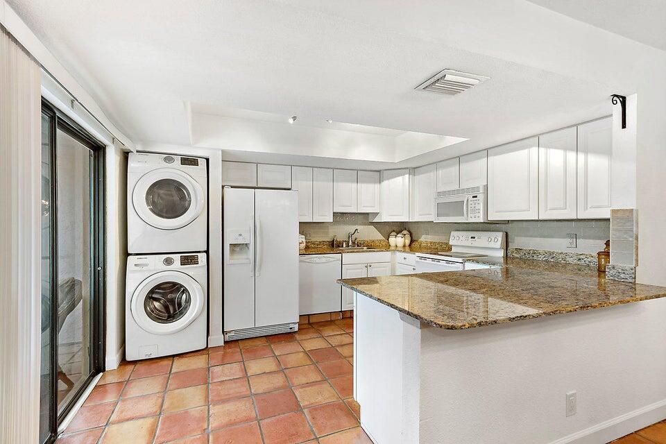 A kitchen with white cabinets, granite countertops, tile flooring, and a stacked washer and dryer — 1608 Shaker Circle, Wellington FL 33414, WELLINGTON, FL