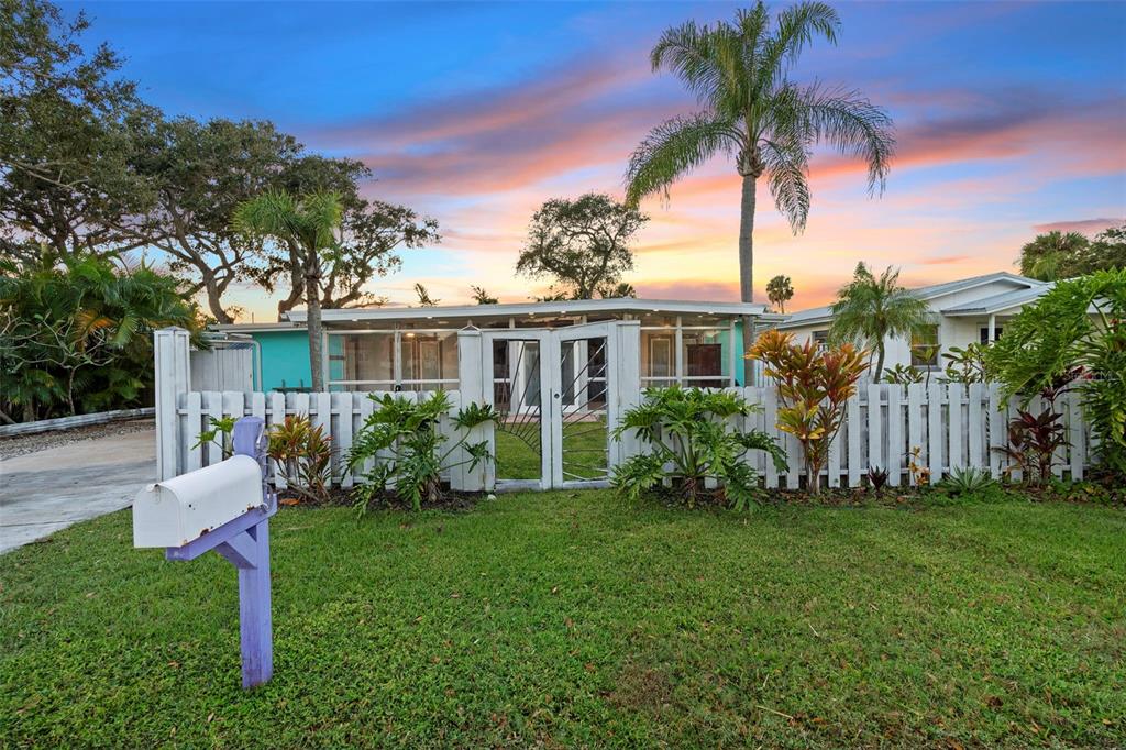 A white picket fence surrounds a house with a screened-in porch under a sunset sky — 650 S PINE STREET, NEW SMYRNA BEACH, FL