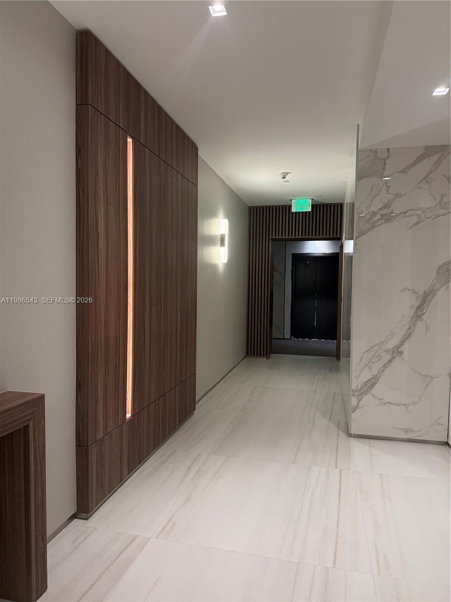 A modern hallway features wood-paneled walls, marble-style flooring, and a recessed doorway with vertical slats — 6365 Collins Ave # 904, Miami Beach FL 33141, MIAMI BEACH, FL