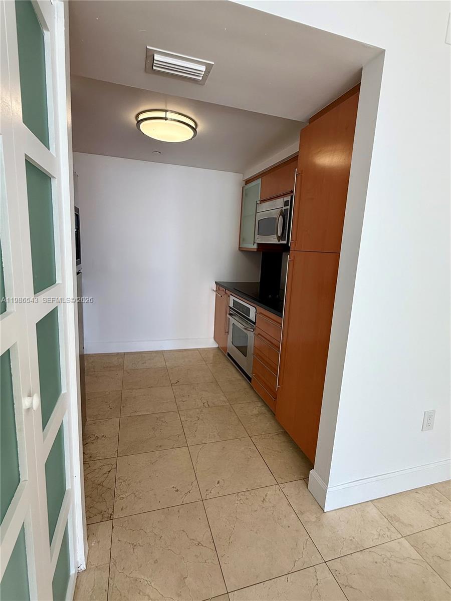 A galley kitchen features wood cabinets, stainless steel appliances, and light-colored tile flooring — 6365 Collins Ave # 904, Miami Beach FL 33141, MIAMI BEACH, FL
