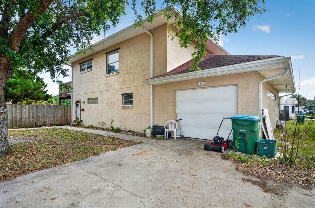 A two-story stucco house with a single-car garage, concrete driveway, and green trash bins — 124 RANDLE AVENUE, OAK HILL, FL