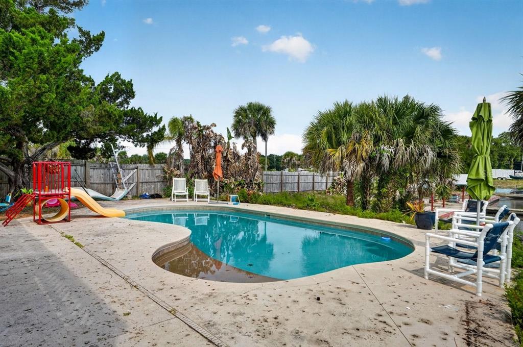 A backyard swimming pool with a slide, patio furniture, and palm trees under a blue sky — 124 RANDLE AVENUE, OAK HILL, FL