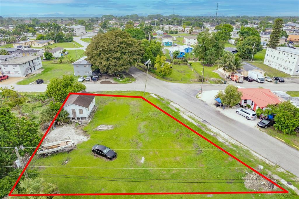 An aerial view shows a vacant, grass-covered corner lot with a small house and boat — 601 SW 6TH STREET, BELLE GLADE, FL