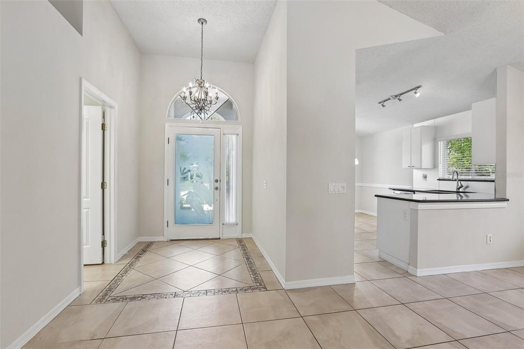 A bright entryway with tile flooring, a chandelier, and a view into the kitchen — 10216 CHARLESTON CORNER ROAD, TAMPA, FL