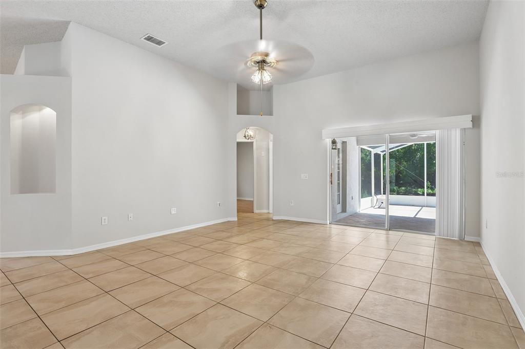 A spacious living room with light-colored tile flooring, vaulted ceilings, and sliding glass patio doors — 10216 CHARLESTON CORNER ROAD, TAMPA, FL