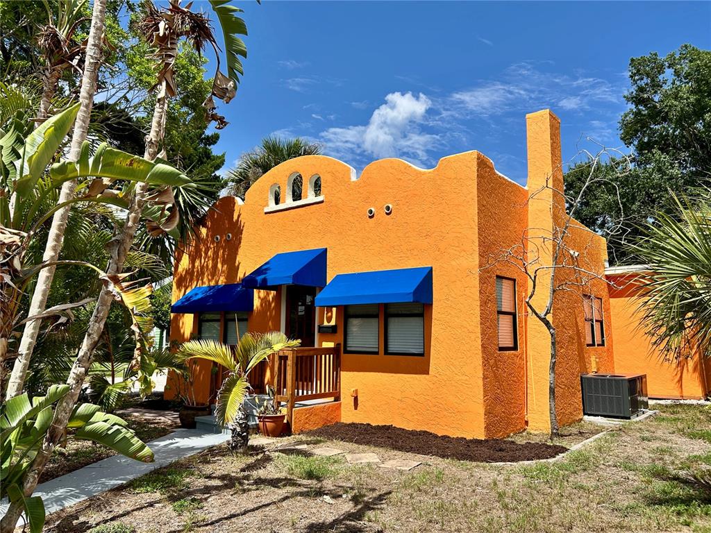 A bright orange stucco house features blue window awnings and a small wooden front porch — 1315 24TH ST W, BRADENTON, FL