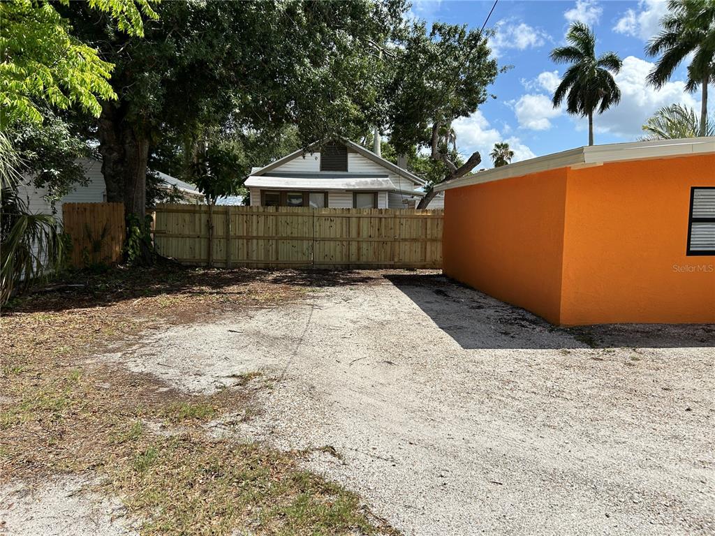 A gravel driveway sits beside an orange building with a wooden fence in the background — 1315 24TH ST W, BRADENTON, FL
