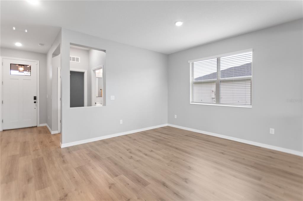 A bright, empty living room features light wood-look flooring, gray walls, and a large window — 12500 ASTON DRIVE, HUDSON, FL