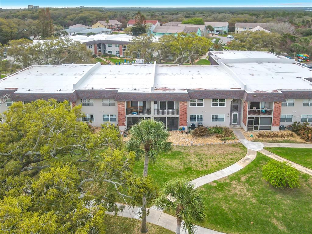 An aerial view of a multi-story apartment building with a flat roof and surrounding landscaping — 3800 SAXON DRIVE UNIT B13, NEW SMYRNA BEACH, FL