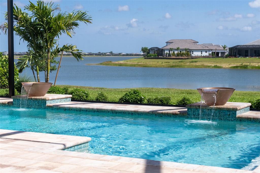 A swimming pool with two water features overlooks a lake and distant houses — 844 BLUE SHELL LOOP, SARASOTA, FL