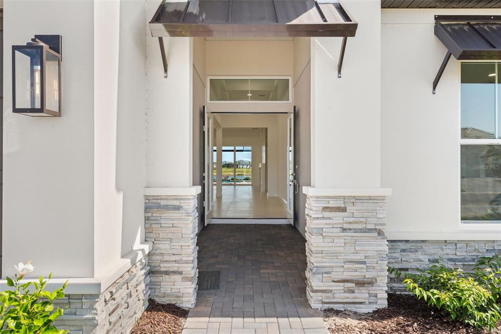 The front entrance features a paved walkway, stone-accented columns, and a view through the doorway — 844 BLUE SHELL LOOP, SARASOTA, FL