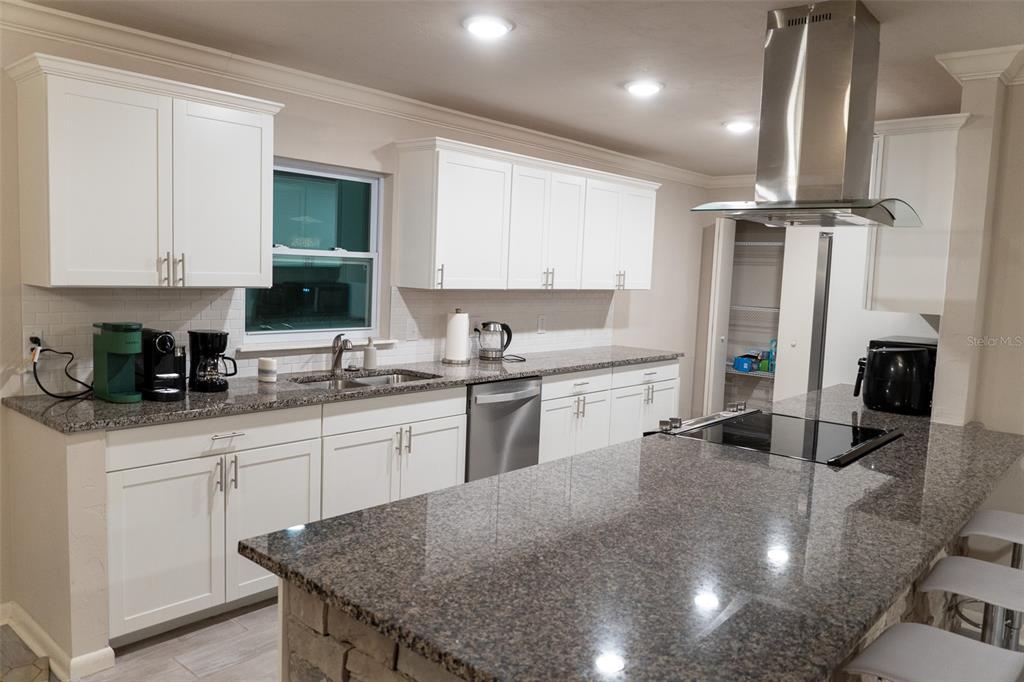 A kitchen features white cabinetry, granite countertops, a stainless steel range hood, and an island — 8221 SW 13TH ROAD, GAINESVILLE, FL