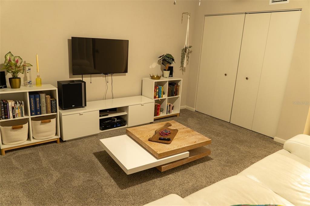 A living room features a television, white media console, shelving units, and a wooden coffee table — 8221 SW 13TH ROAD, GAINESVILLE, FL