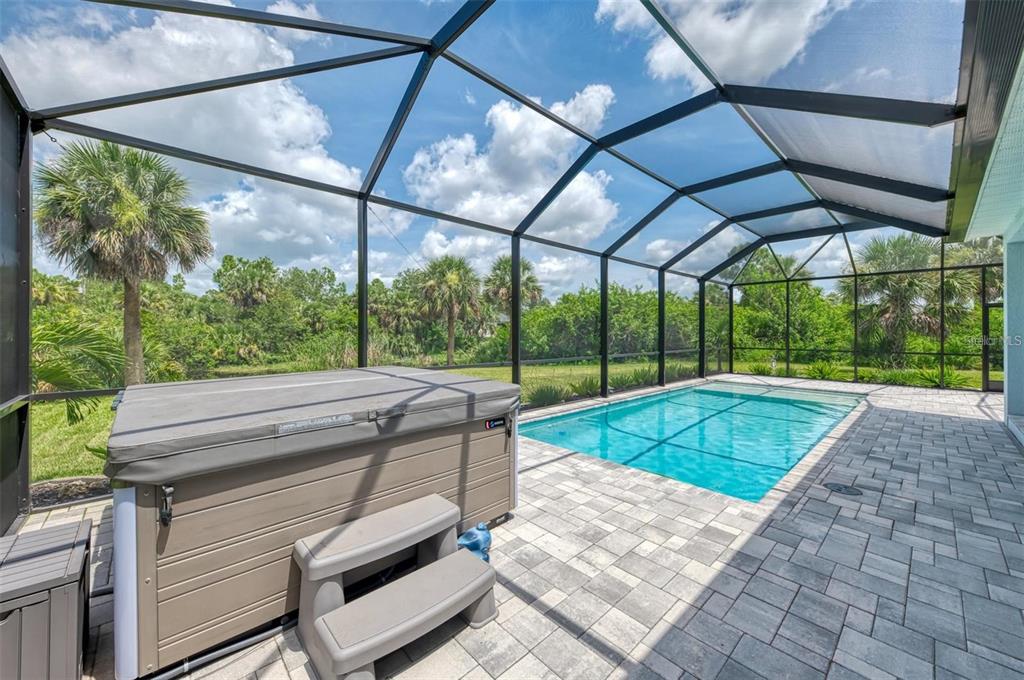 A screened-in pool area features a hot tub, stone paver patio, and lush backyard landscaping — 2129 LORRAINE DRIVE, PORT CHARLOTTE, FL