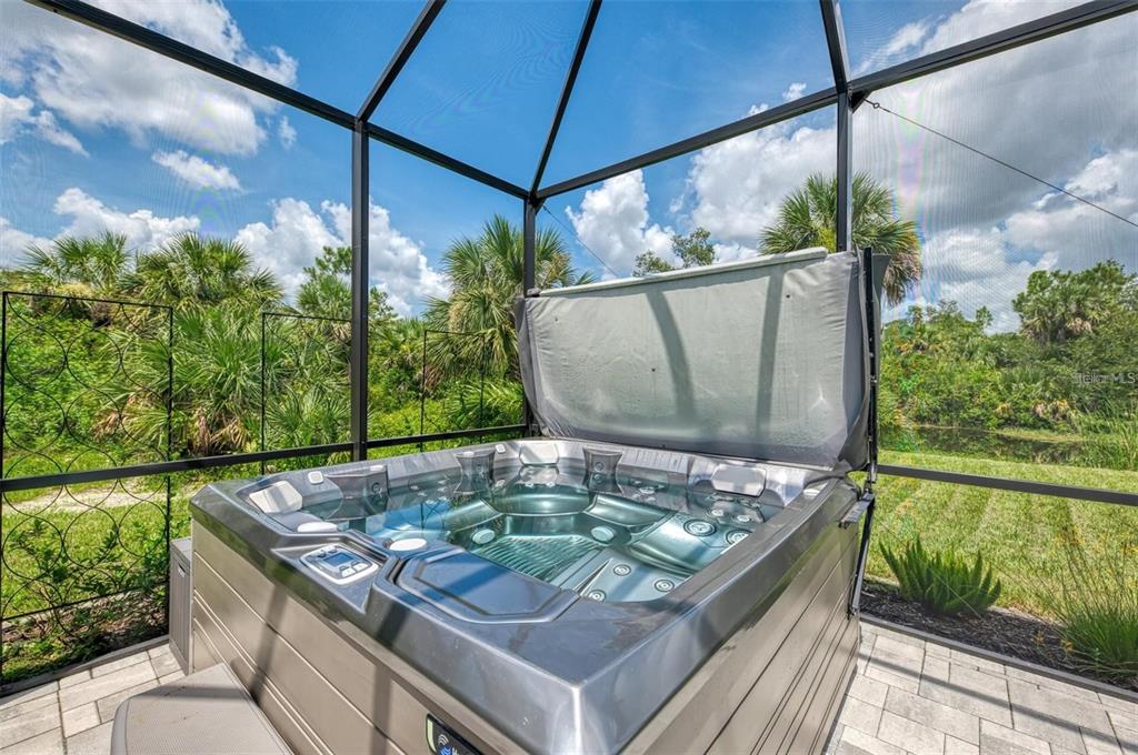 A hot tub sits on a paved patio inside a screened-in enclosure overlooking greenery — 2129 LORRAINE DRIVE, PORT CHARLOTTE, FL
