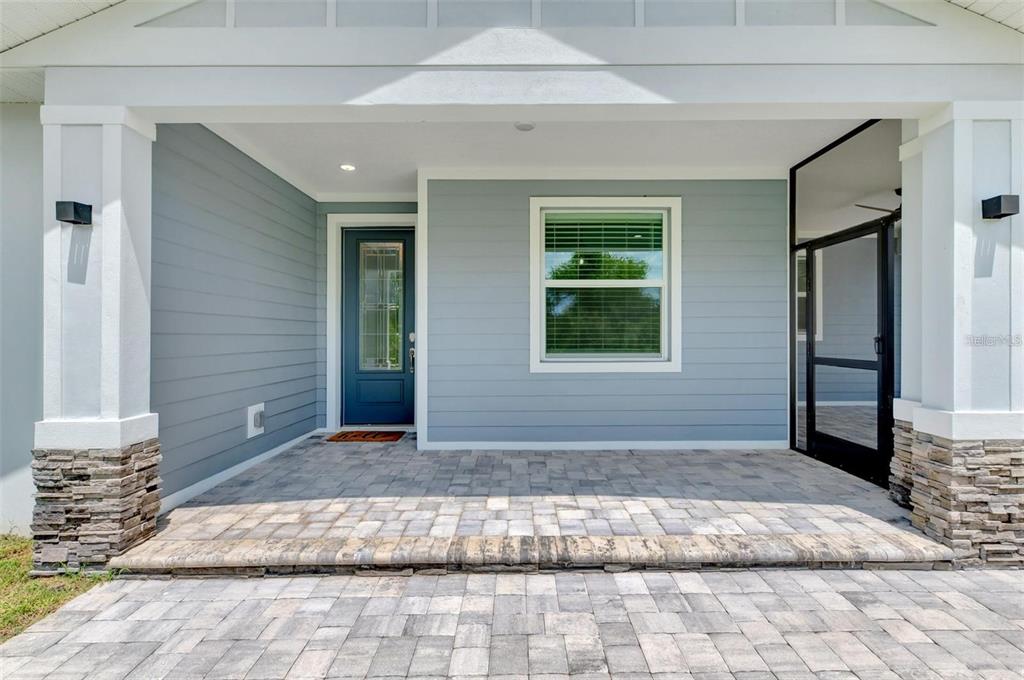 A covered front porch features light blue horizontal siding, a dark door, and paver flooring — 2129 LORRAINE DRIVE, PORT CHARLOTTE, FL