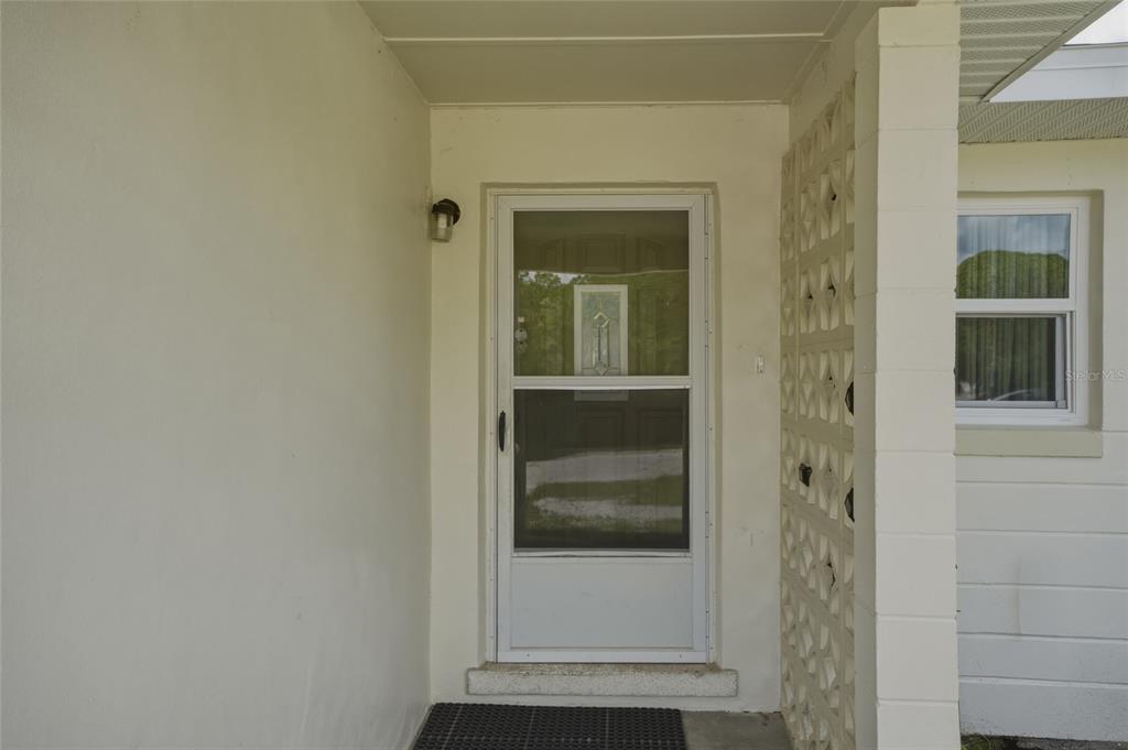 A white front door with a screen door sits on a covered concrete porch — 965 ALLENDALE STREET, TITUSVILLE, FL