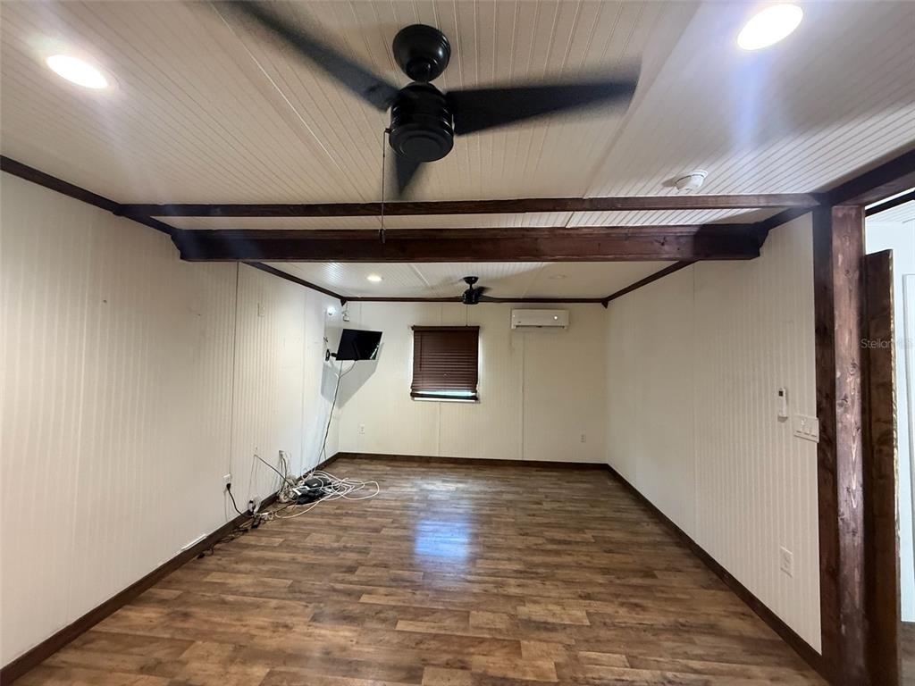 An empty room features wood-look flooring, white paneled walls, exposed ceiling beams, and two ceiling fans — 18312 HOLISTER RD, ORLANDO, FL