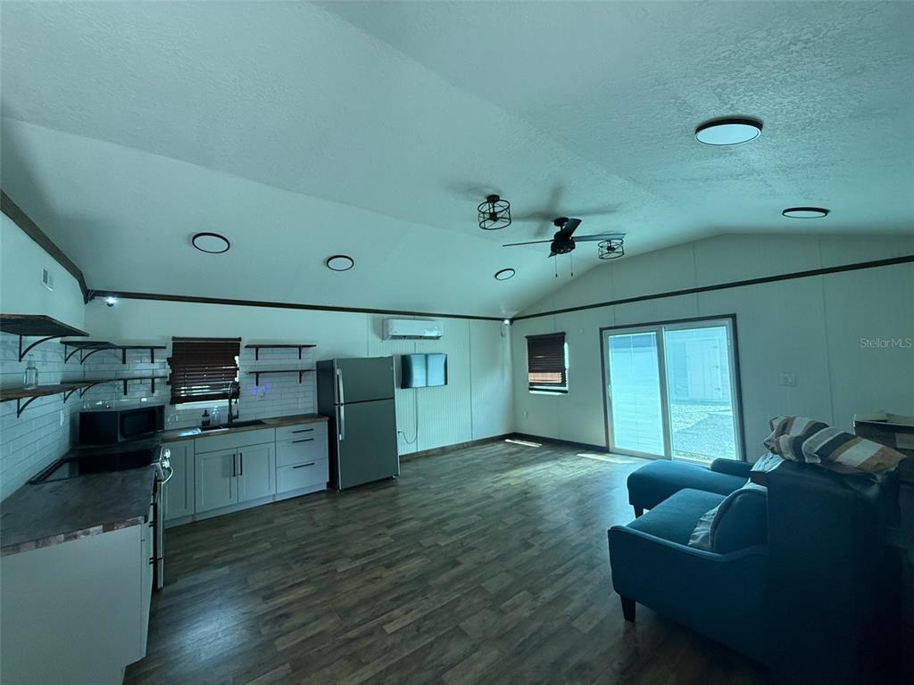 An open-concept living room and kitchen area features light gray cabinets, wood-look flooring, and vaulted ceilings — 18312 HOLISTER RD, ORLANDO, FL