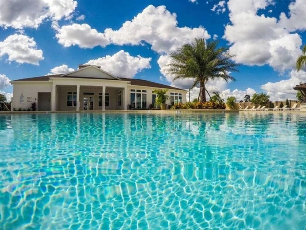 A swimming pool sits in the foreground with a clubhouse building and palm tree behind it — 8933 SHINE DRIVE, KISSIMMEE, FL