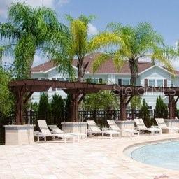 A wooden pergola shades lounge chairs on a paved pool deck in front of a house — 8933 SHINE DRIVE, KISSIMMEE, FL