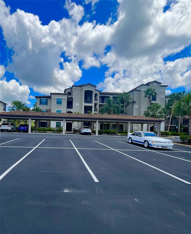 A white car is parked in front of a multi-story apartment building with covered parking — 17108 VARDON TERRACE UNIT 401, BRADENTON, FL